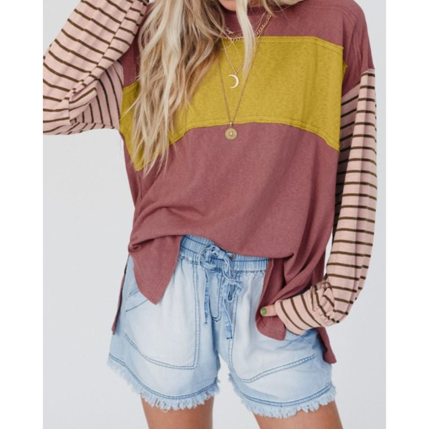 Person wearing a color-blocked long-sleeve top with striped sleeves and denim shorts on a white background