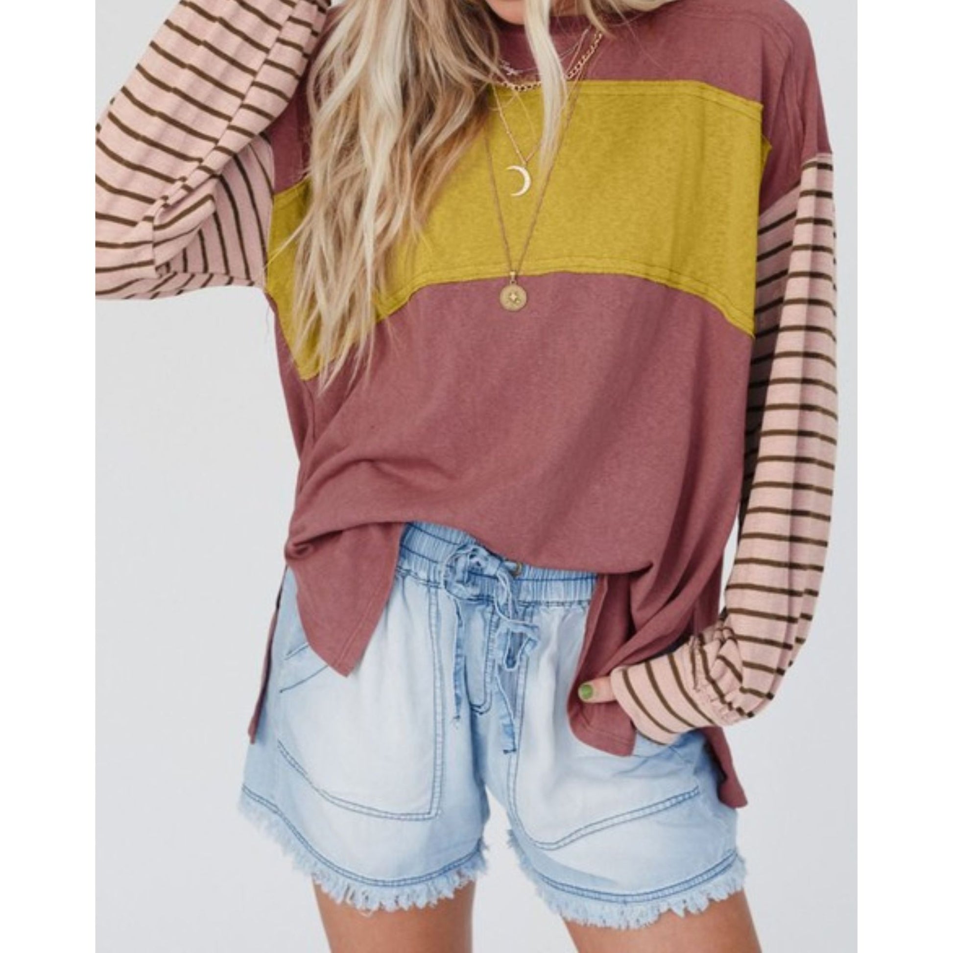 Person wearing a color-blocked long-sleeve top with striped sleeves and denim shorts on a white background