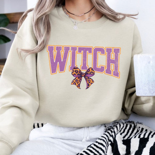Beige sweatshirt with 'WITCH' in purple and a bow graphic, worn by a person.