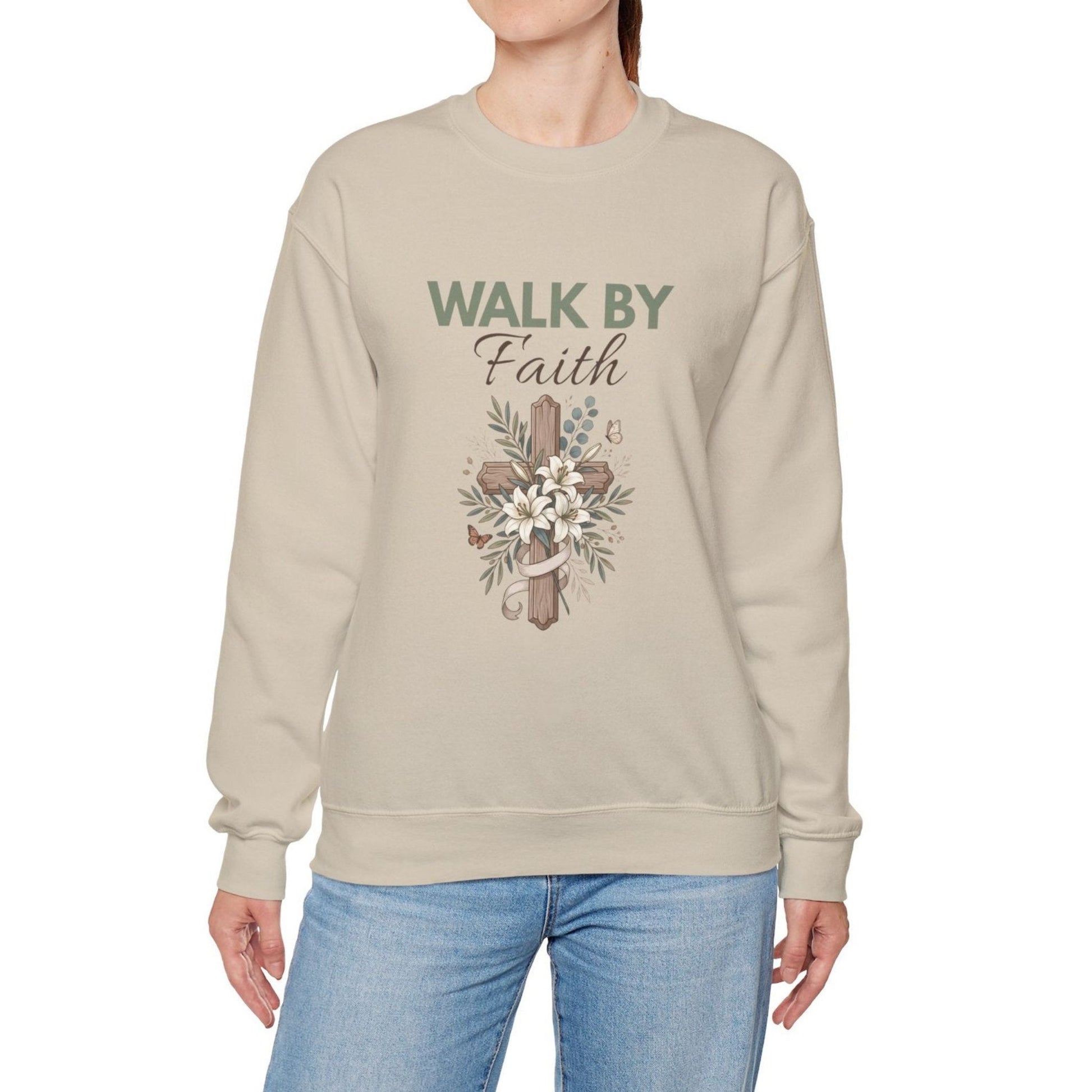 A woman is wearing a sand colored crewneck hoodie with 'WALK BY Faith' on the front.