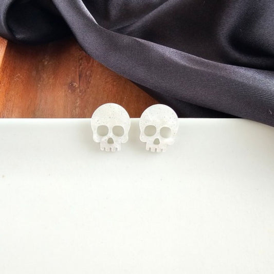 White skull-shaped earrings on a white surface with a dark fabric background