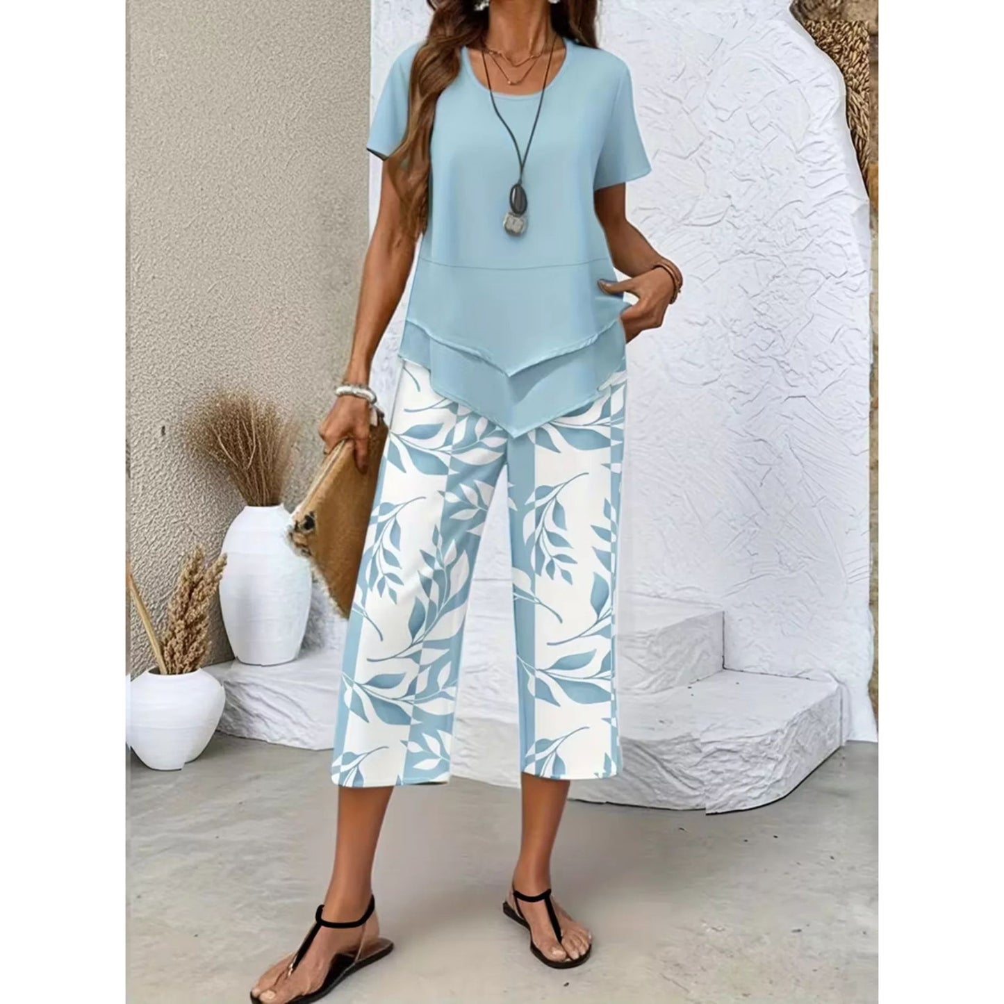 A woman is wearing a Sky Blue layered top and leaf print cropped pants.