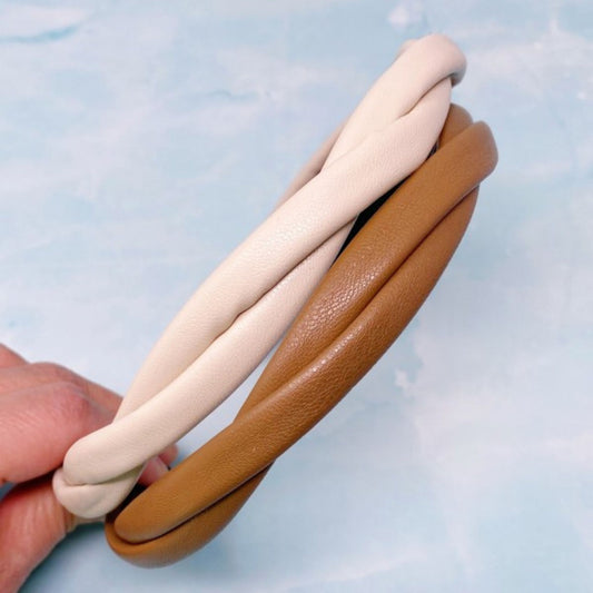 Two bracelets, one beige and one brown, held against a light blue background.