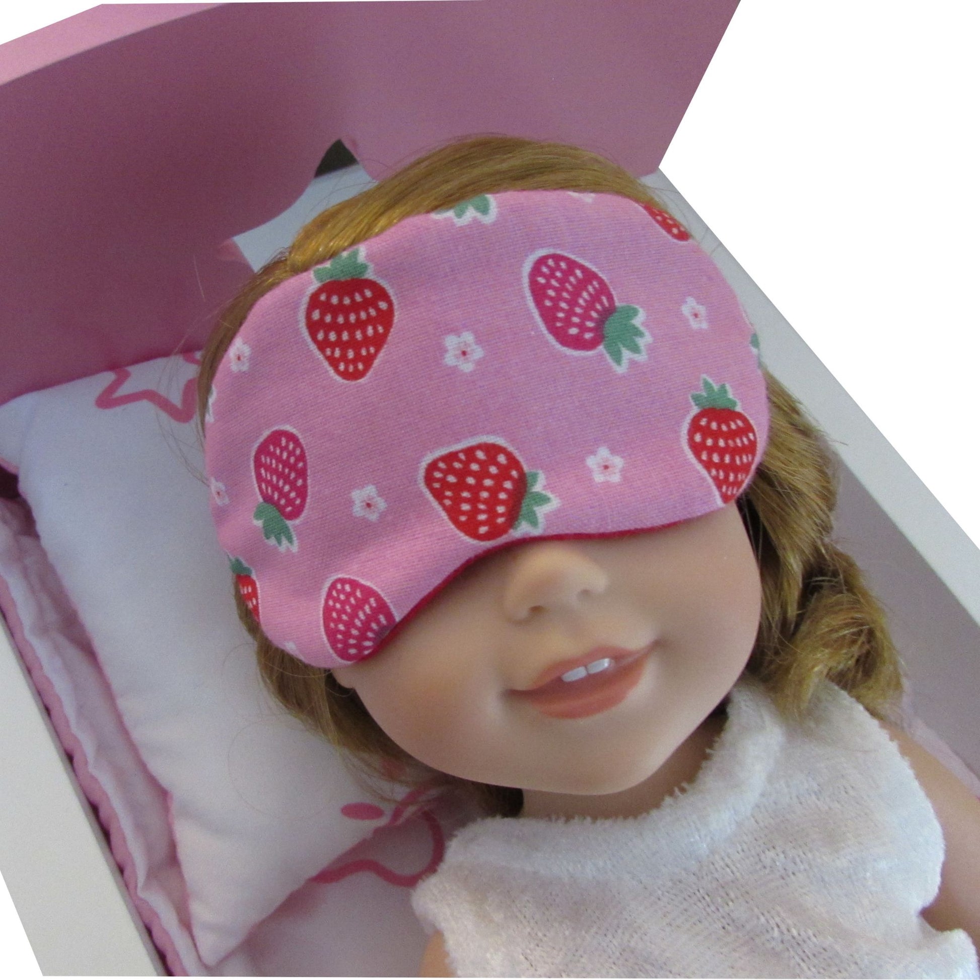Doll wearing a pink sleep mask with strawberry pattern on a white background