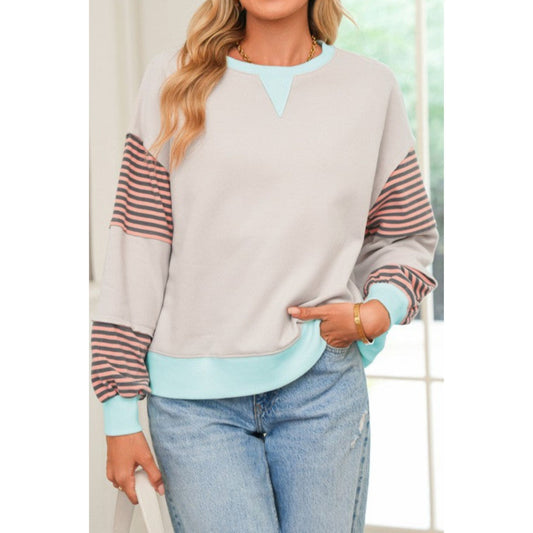 Woman wearing a gray sweater with colorful sleeves and light blue jeans indoors.