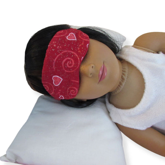 Doll wearing a red patterned sleep mask and white robe on a white background