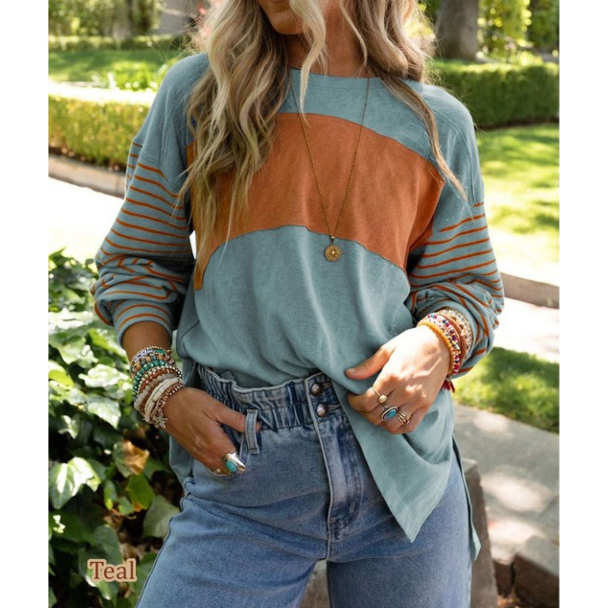 Person wearing a teal and orange color-blocked sweater with denim shorts outdoors.