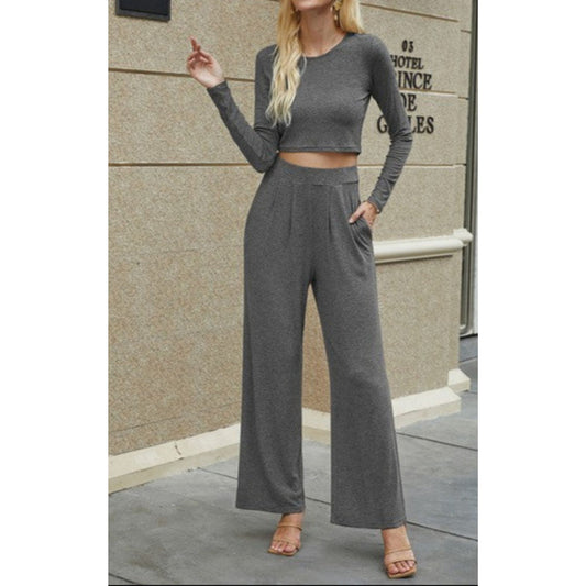 Woman wearing a gray long-sleeve top and wide-leg pants standing against a beige wall.