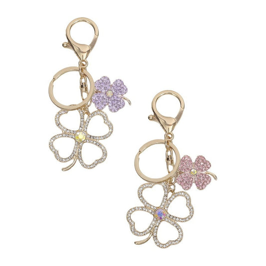 Two gold keychains with clover and flower designs on a white background