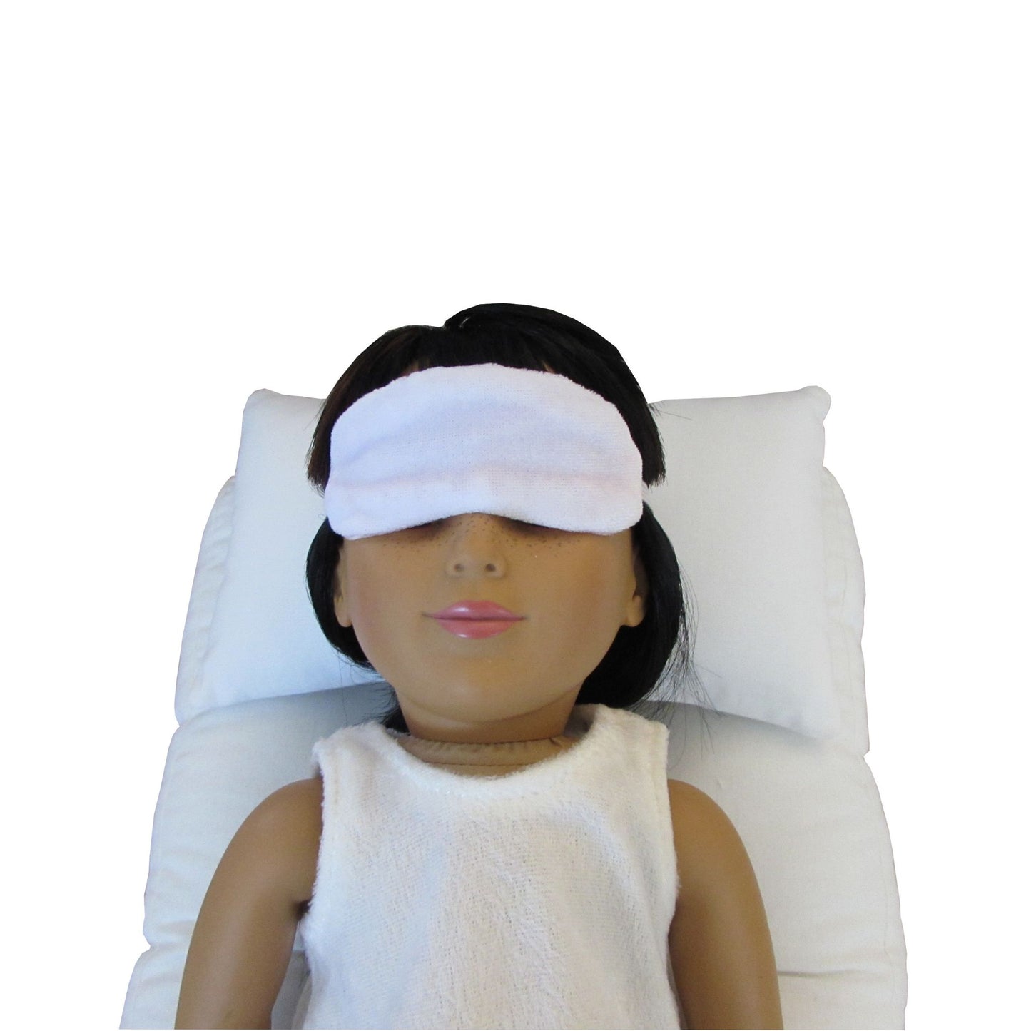 An 18-inch doll is wearing a white stretch velvet sleep mask while lying on a white doll pillow and a white doll mattress.