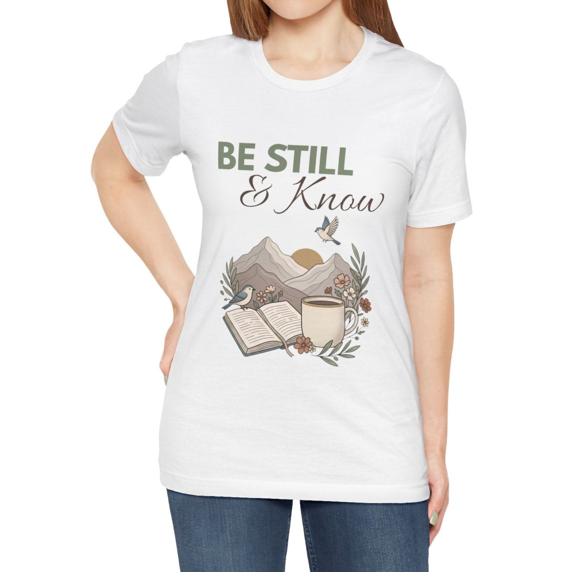 White t-shirt with 'Be Still & Know' design featuring a book, cup, and mountains on a white background.