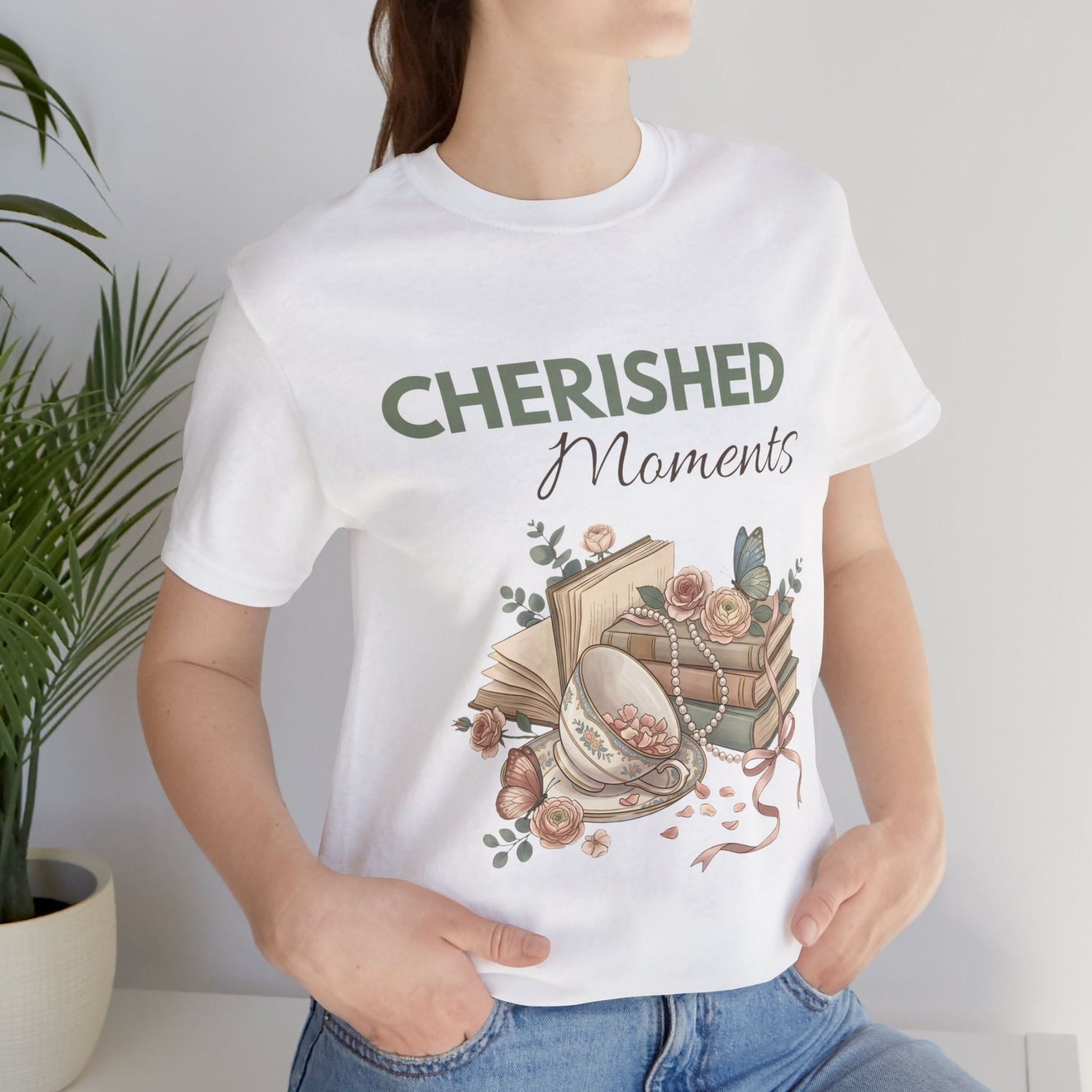 A woman is standing by a plant with a white t-shirt with 'CHERISHED Moments' on the front.