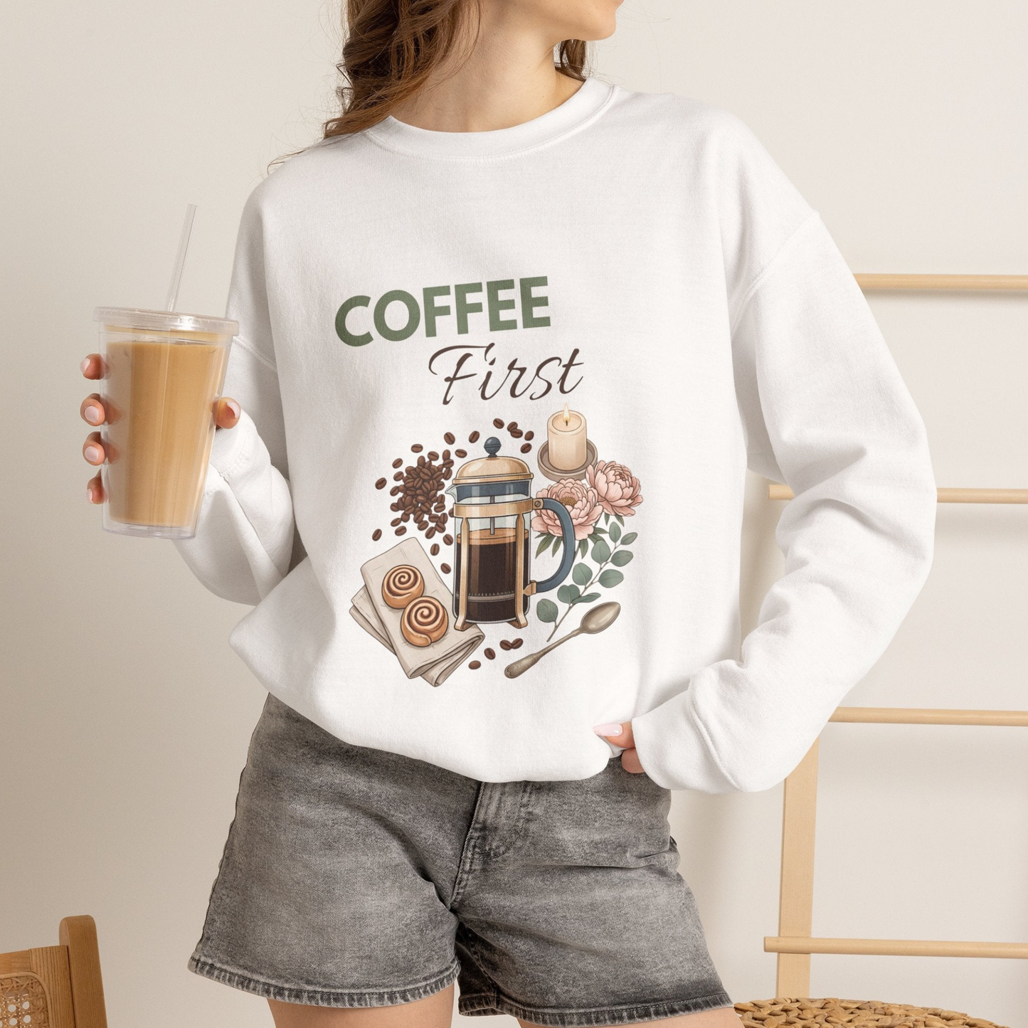 A woman is wearing a white sweatshirt with 'COFFEE First' on the front and is holding an iced coffee.