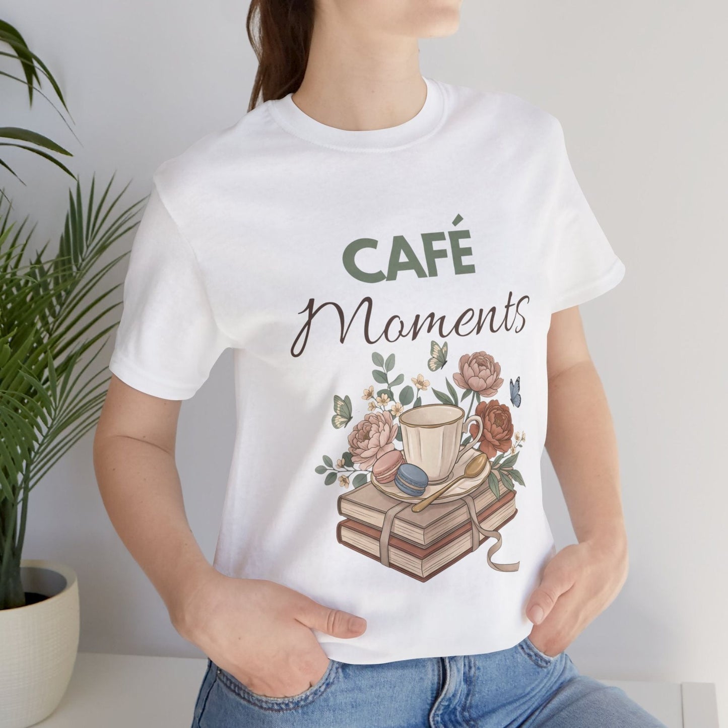 Person wearing a white t-shirt with 'Café Moments' design featuring a coffee cup and books.