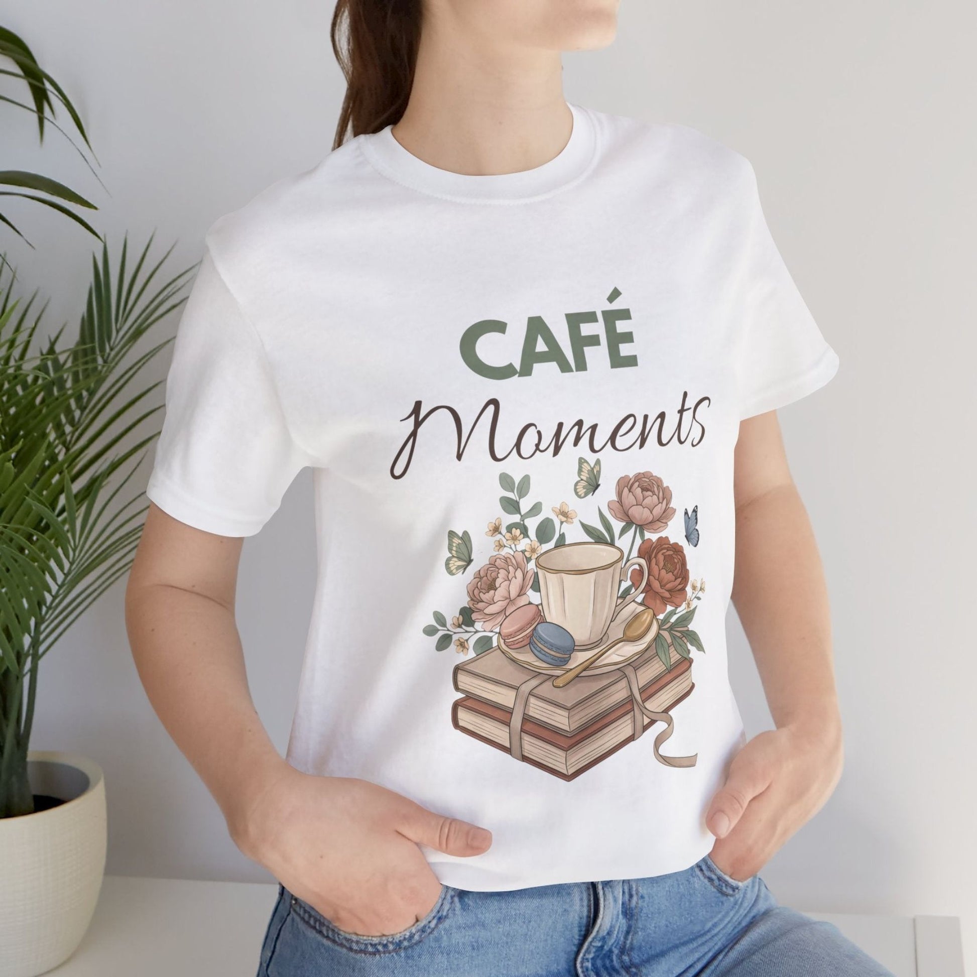 Person wearing a white t-shirt with 'Café Moments' design featuring a coffee cup and books.