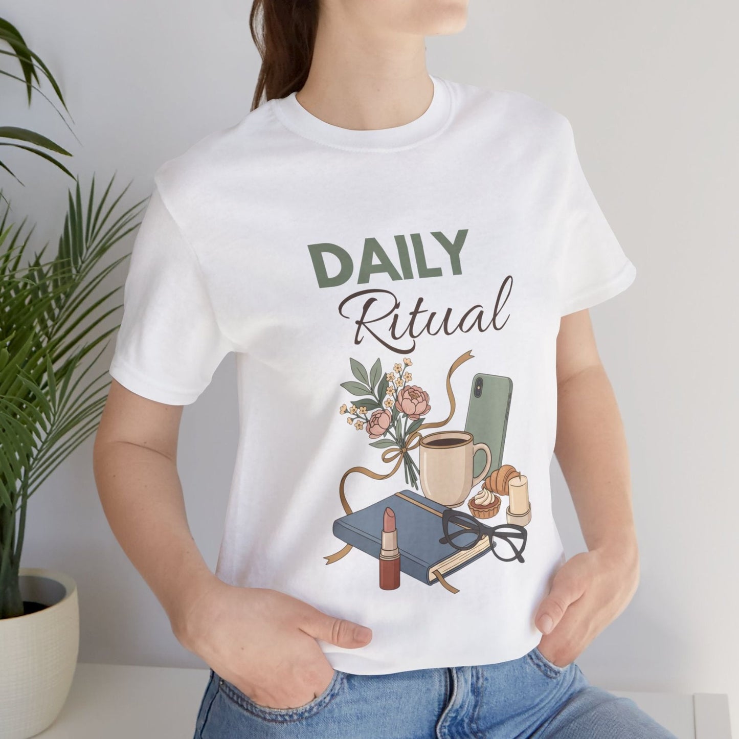 Person wearing a white t-shirt with 'Daily Ritual' design, featuring a cup, flowers, and books.