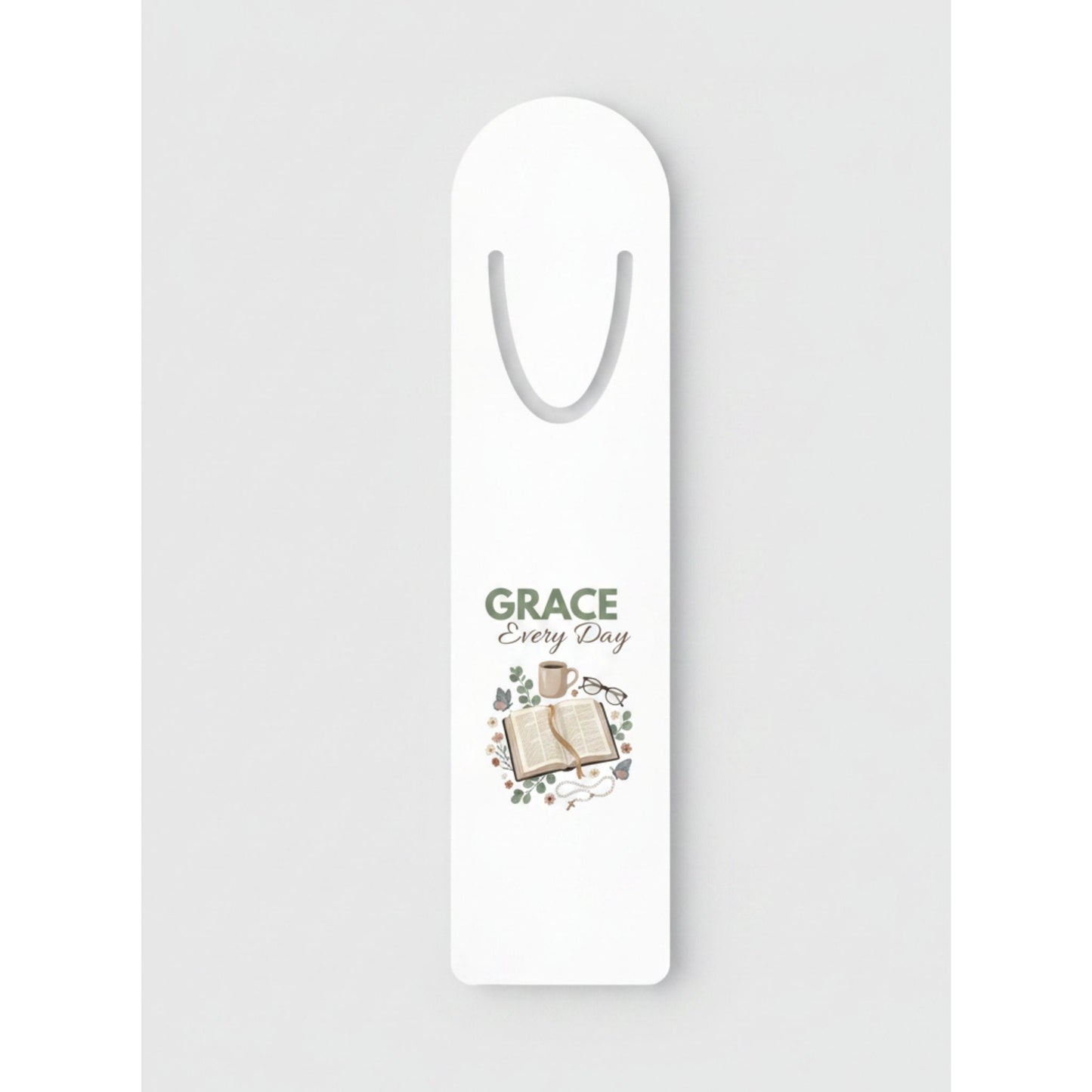 A white bookmark with a printed design in the center featuring the words 'GRACE Every Day' above an illustration of an open book and small decorative elements.