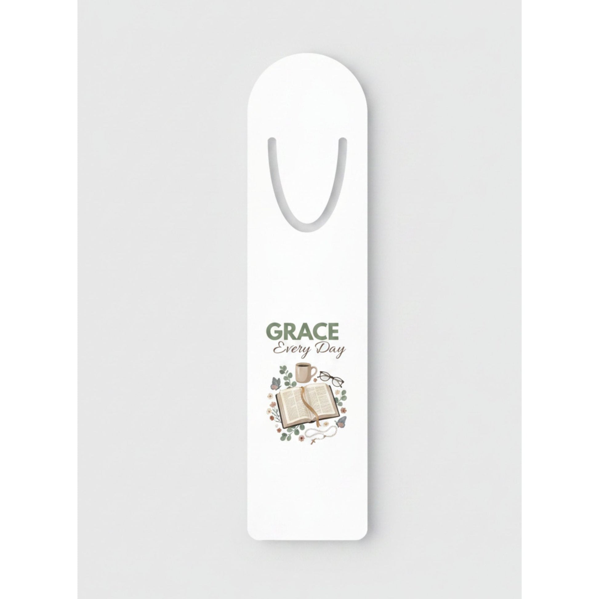 A white bookmark with a printed design in the center featuring the words 'GRACE Every Day' above an illustration of an open book and small decorative elements.
