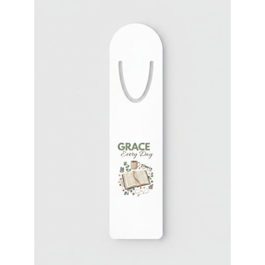 A white bookmark with a printed design in the center featuring the words 'GRACE Every Day' above an illustration of an open book and small decorative elements.