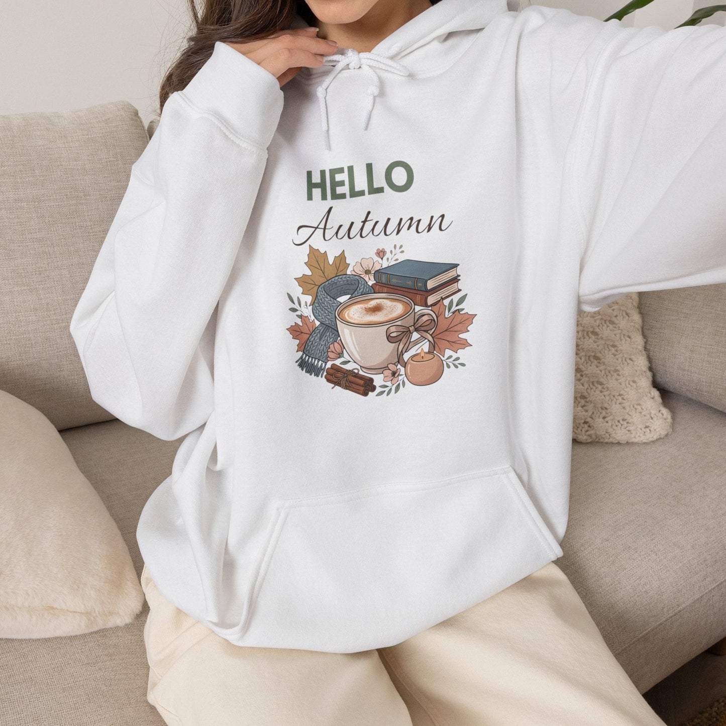 A woman is wearing a white hooded sweatshirt with 'HELLO Autumn' on the front and is sitting on a couch.