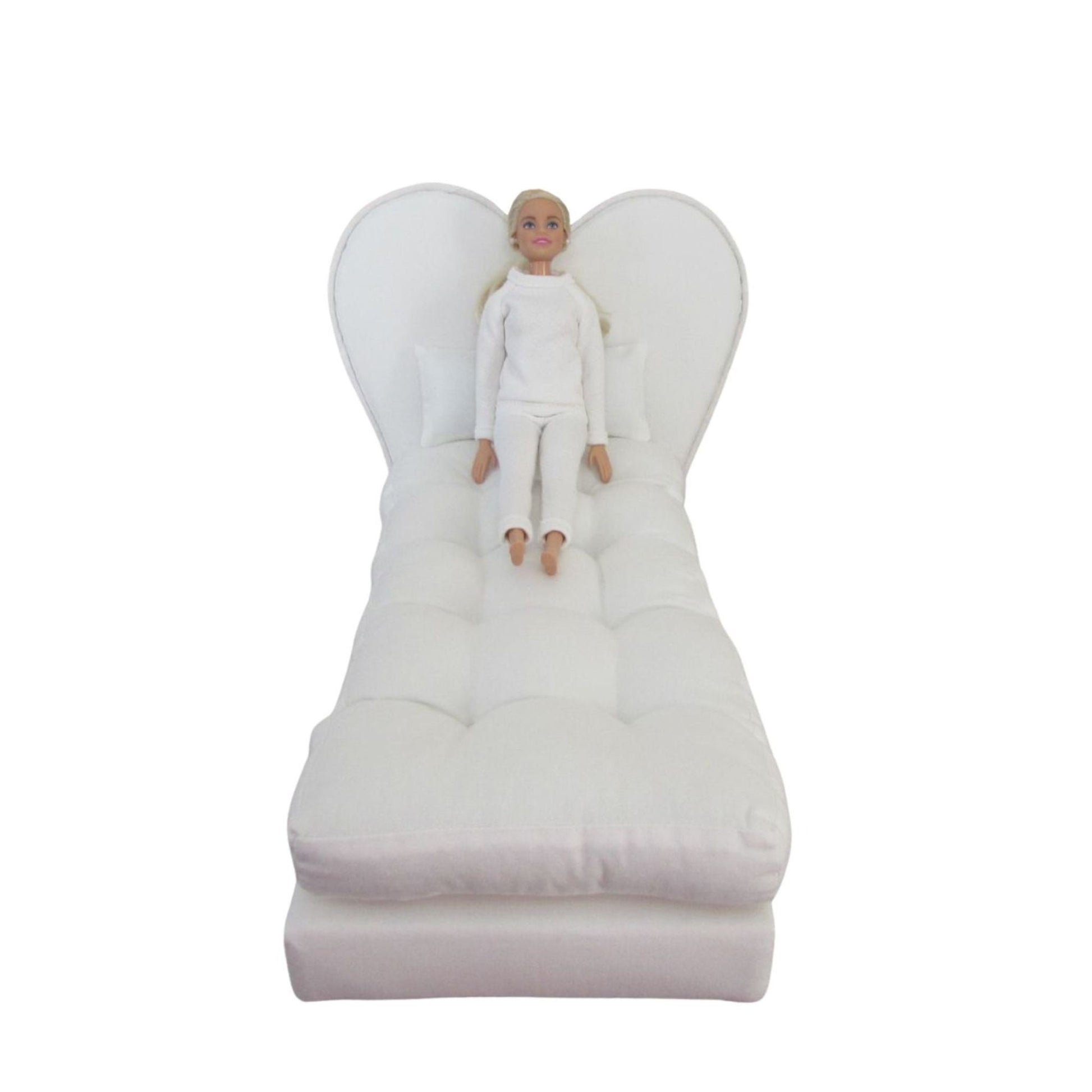 White angel-shaped pillow with a doll sitting on it against a white background