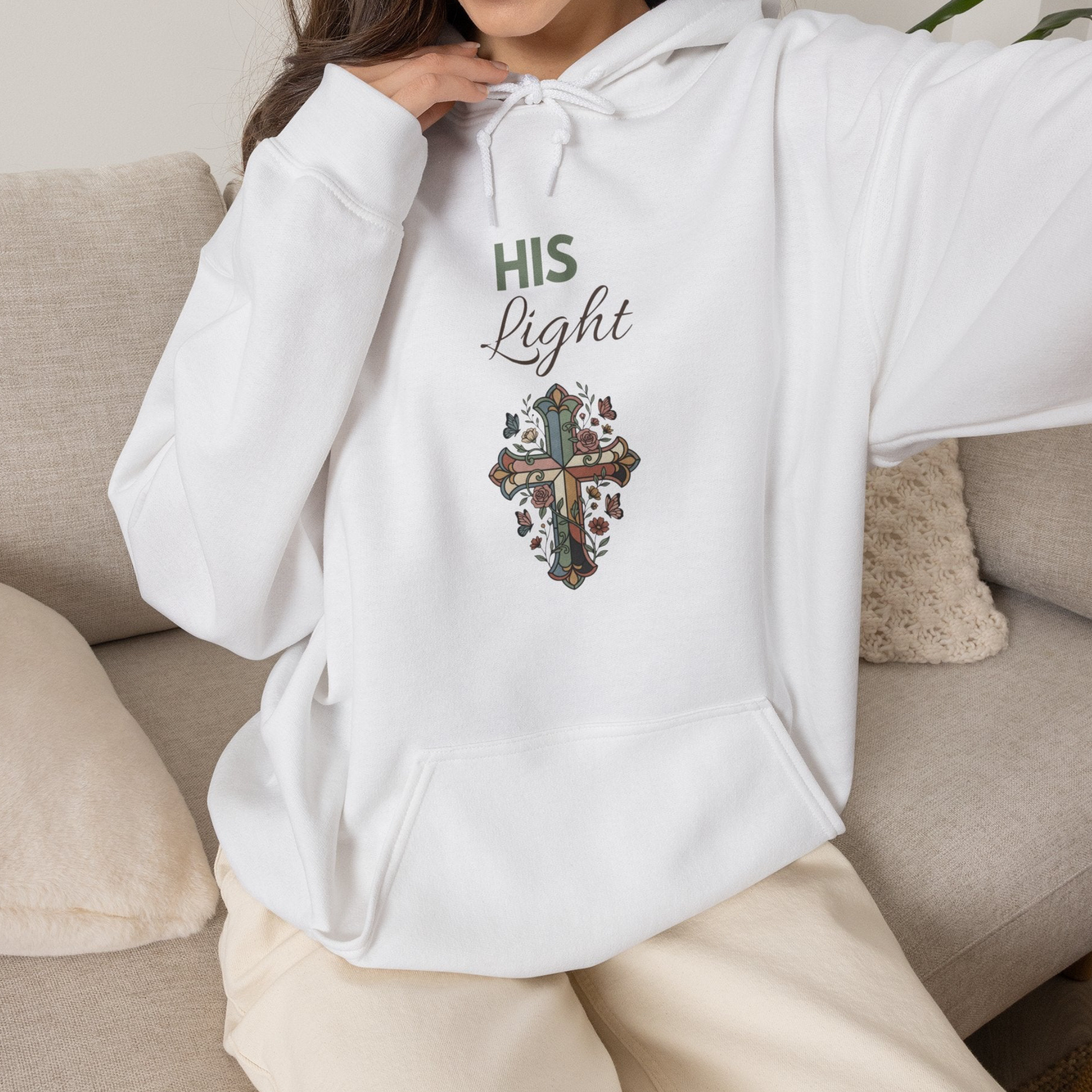 A woman is wearing a white hooded sweatshirt with 'His Light' on the front and is sitting on a couch.