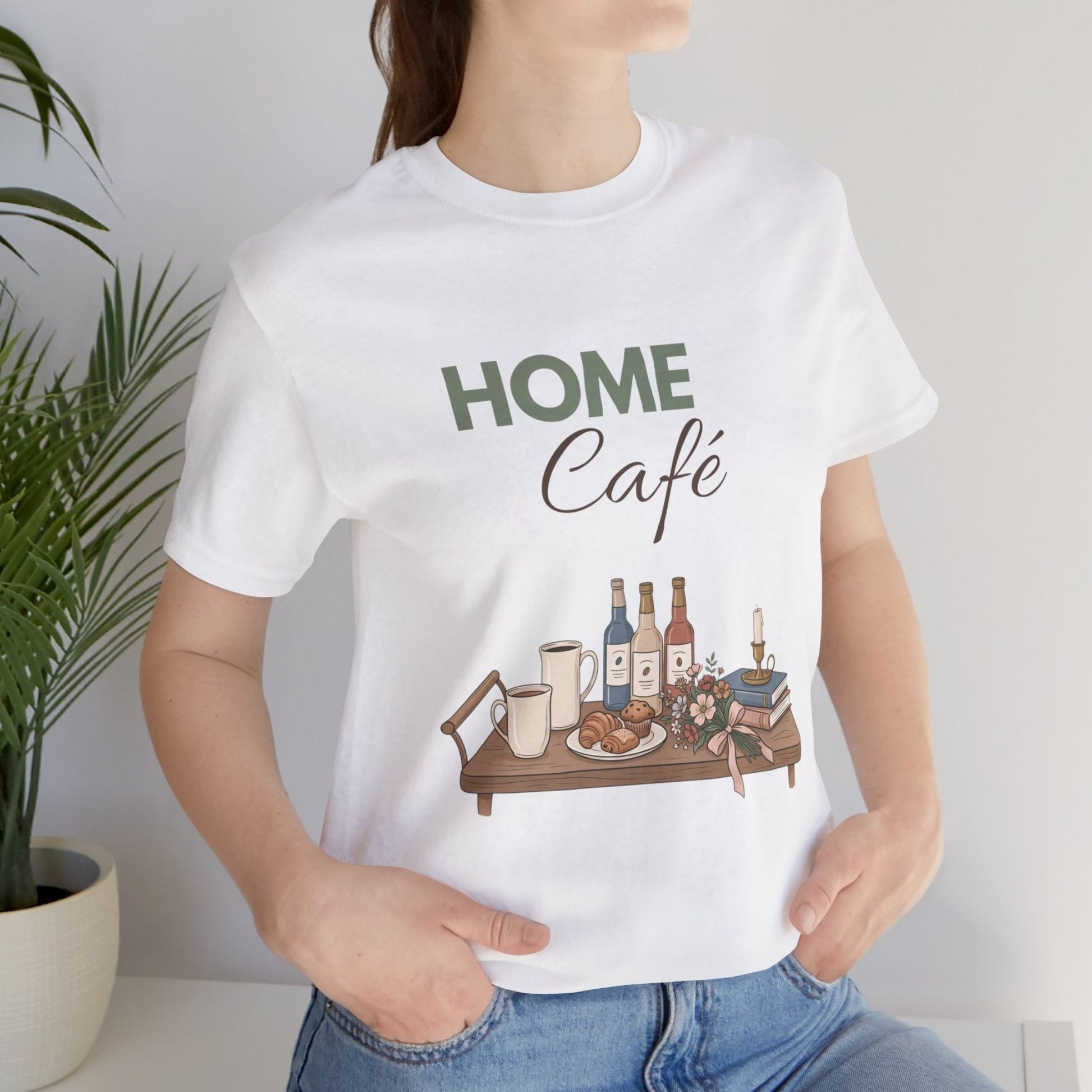 Person wearing a white t-shirt with 'HOME Café' design, featuring a table with bottles and food.