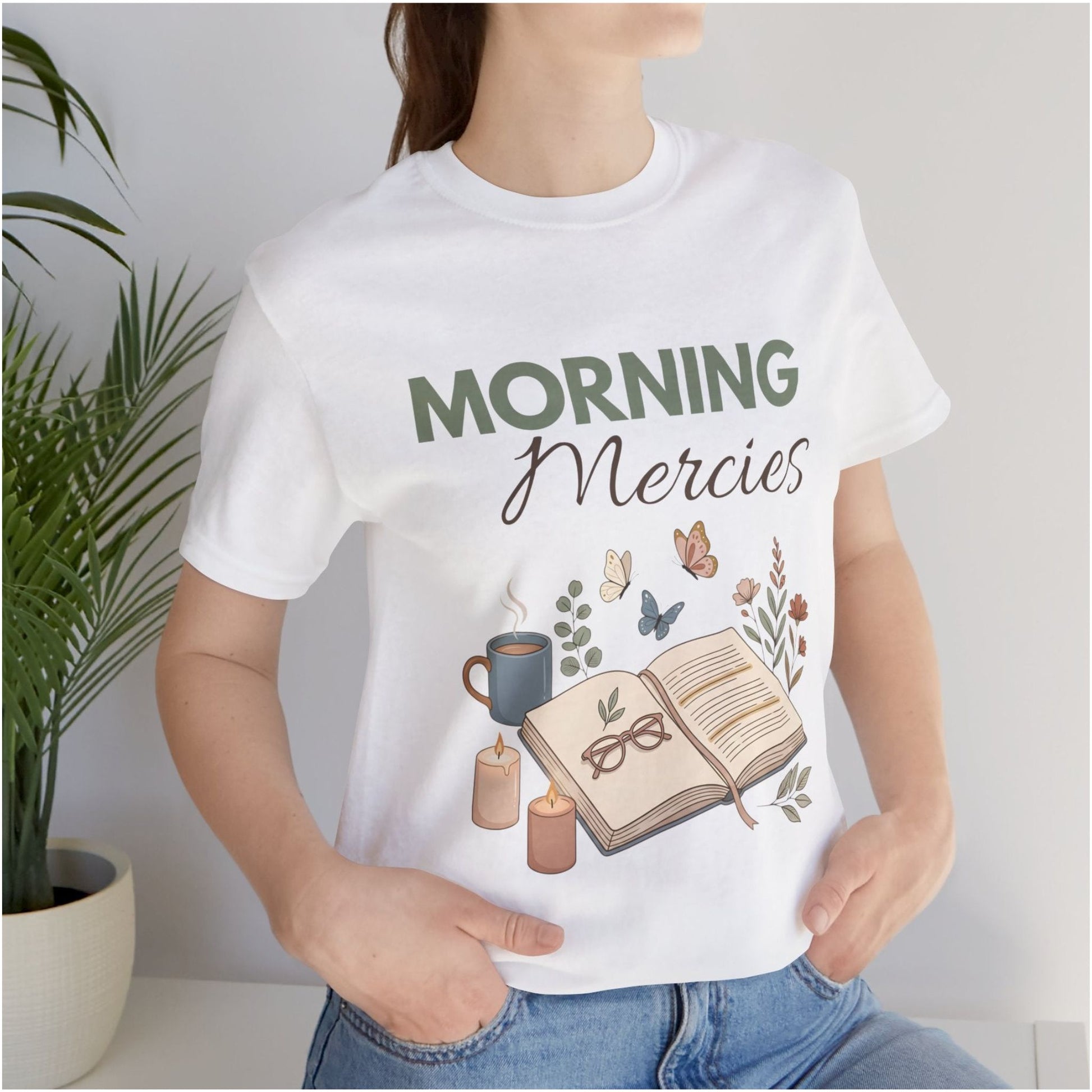 Person wearing a white t-shirt with 'Morning Mercies' design, including a book, coffee cup, and candles.