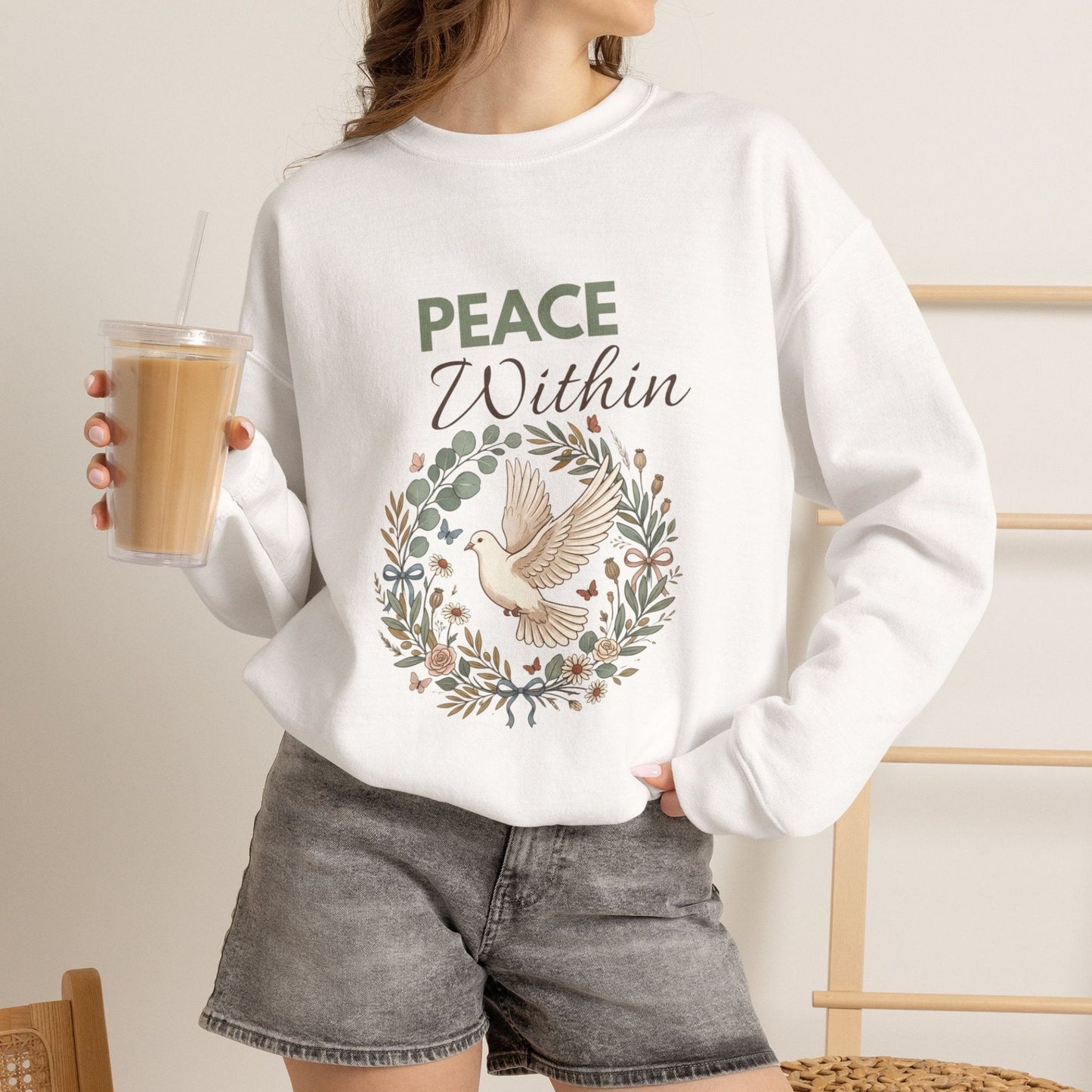 A woman is wearing a white sweatshirt with 'PEACE Within' on the front and holding an iced coffee.
