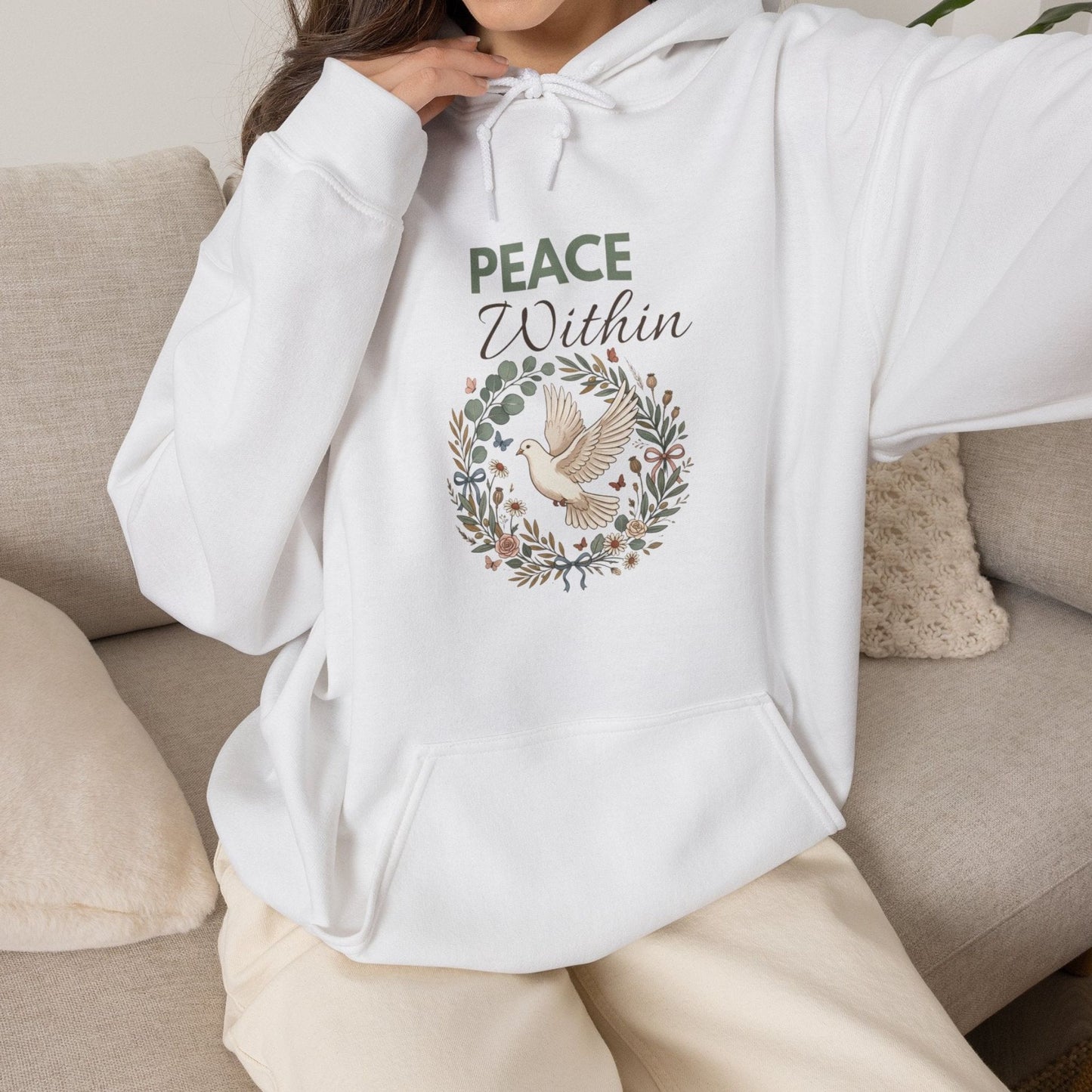 A woman is wearing a white hooded sweatshirt with 'PEACE Within' on the front and is sitting on a couch.