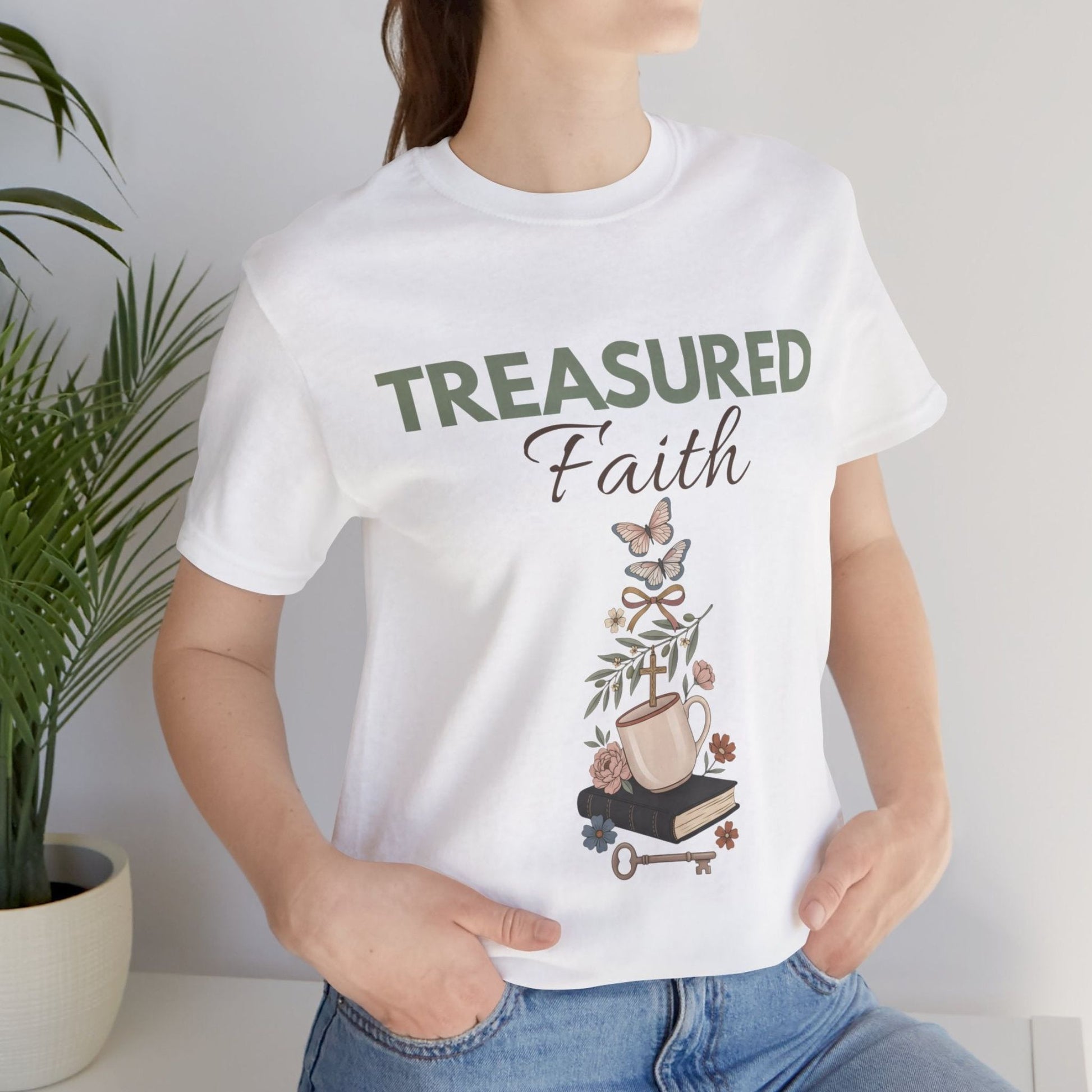 Person wearing a white t-shirt with 'TREASURED Faith' design, standing next to a plant.