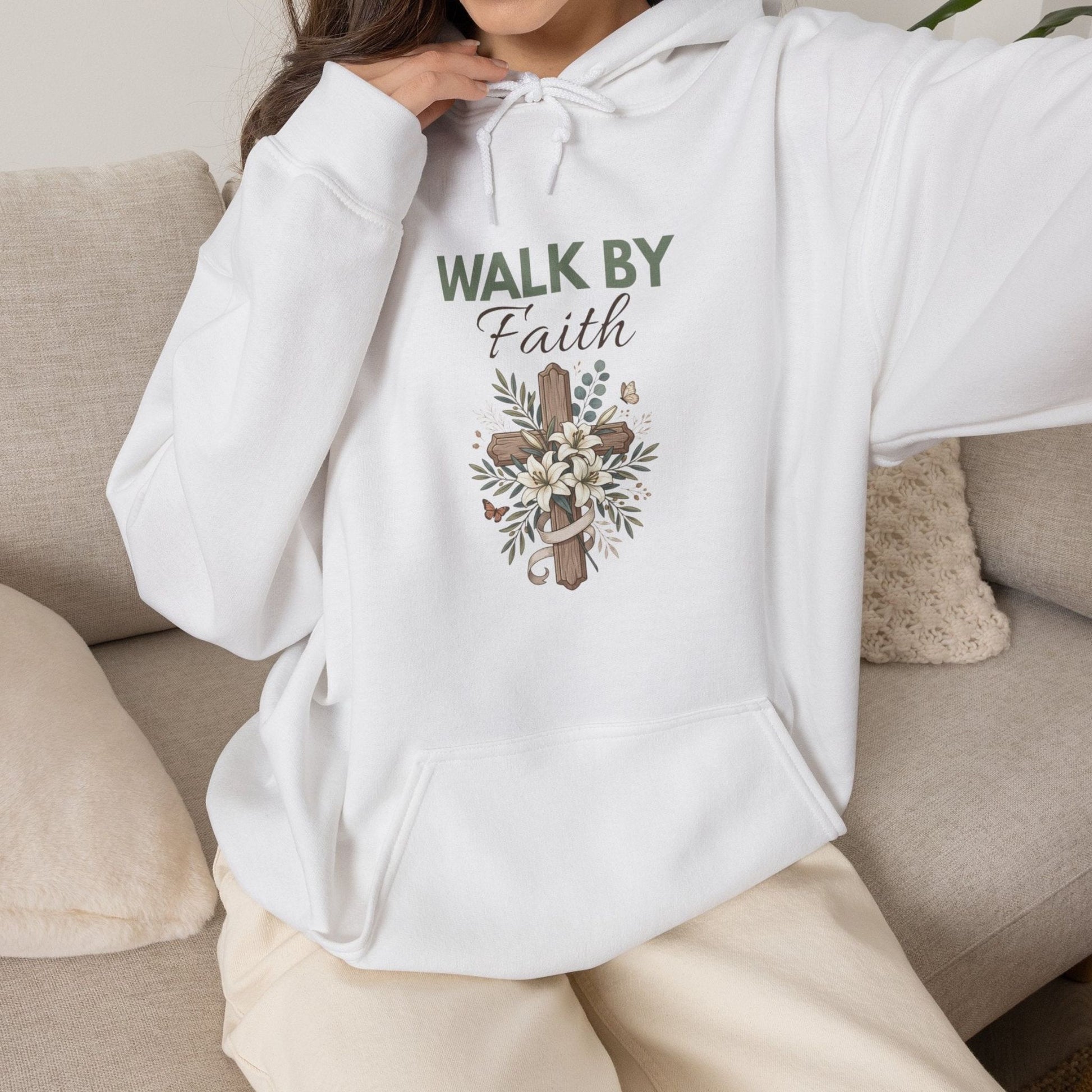 A woman sitting on a couch while wearing a white hooded sweatshirt with 'WALK BY Faith' on the front.