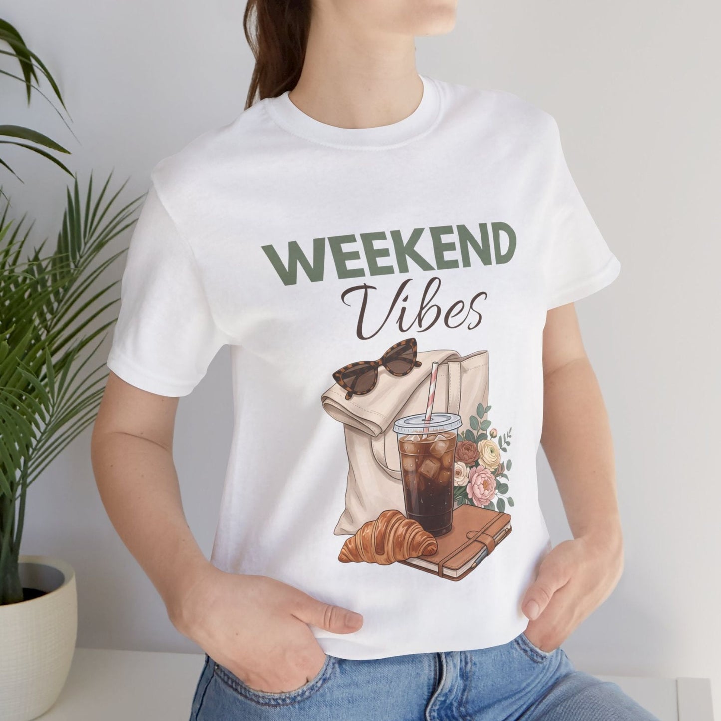 Person wearing a white t-shirt with 'Weekend Vibes' design featuring a coffee cup, croissant, and flowers.