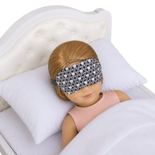 Doll wearing a patterned sleep mask on a bed