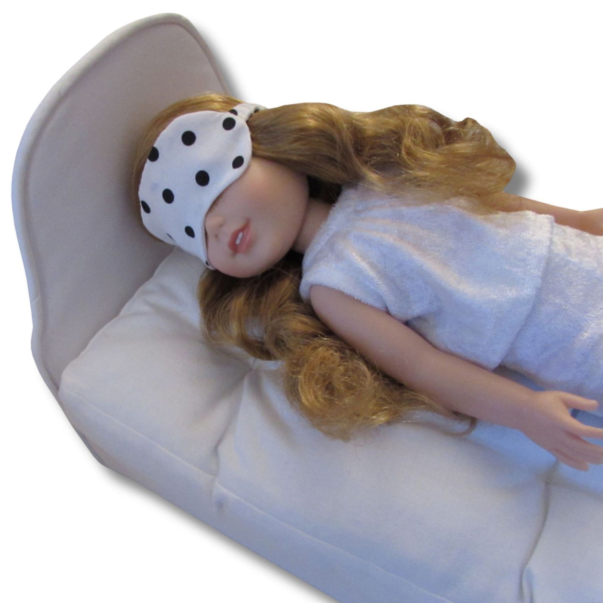 Doll wearing a white polka dot eye mask on a white background