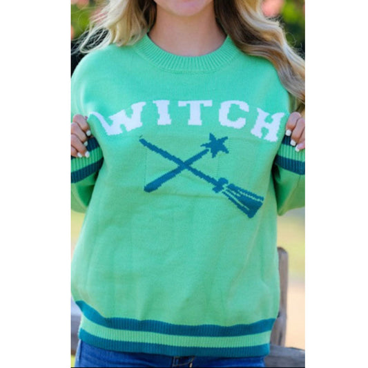 Green sweater with 'WITCH' and broomsticks printed on it, worn by a person.