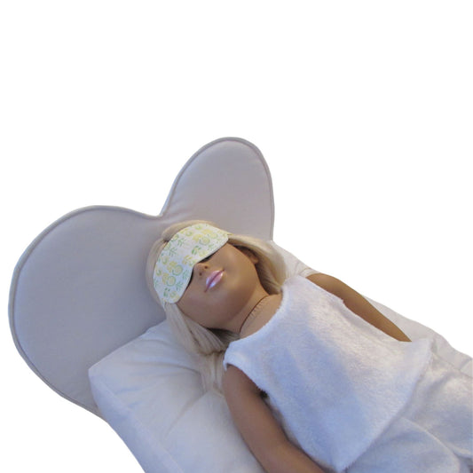 An 18-inch doll wearing a sleep mask while lying on a heart doll bed.