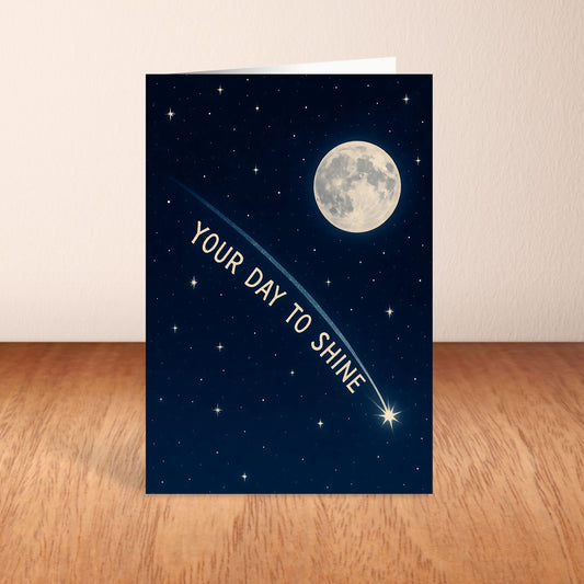 Greeting card with a night sky design, moon, and stars on a wooden surface.